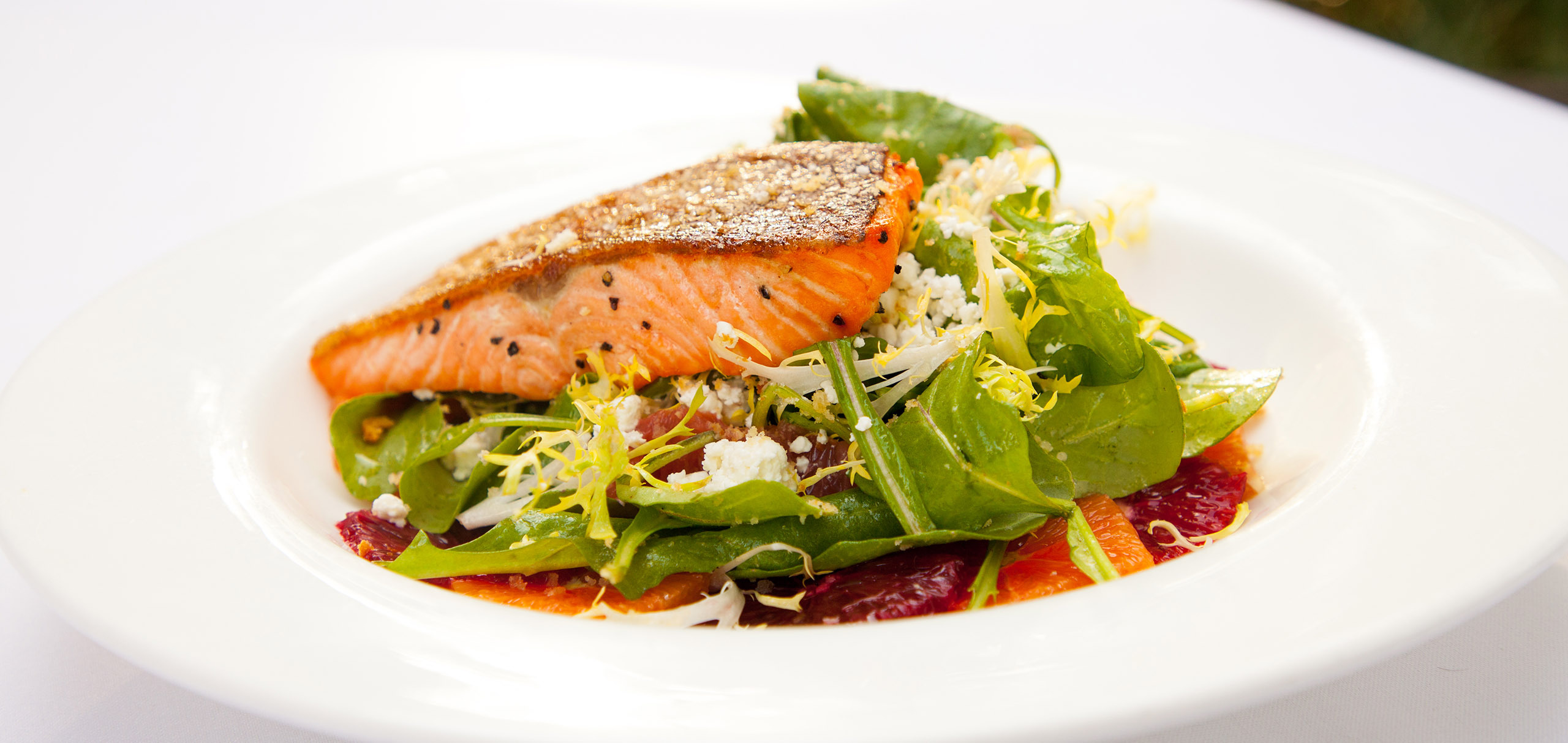 Photo of grilled salmon on top of a green salad with balsamic dressing on a white plate.